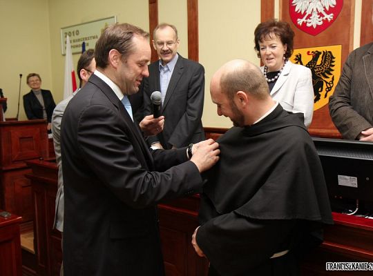 Grafika #1: Złota odznaka „Za opiekę nad zabytkami dla o. Tomasza Janka
